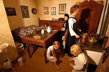 Szene in der Ausstellung: Eine Familie in einer Arbeiterwohnung. Bett, Tisch und Herd befinden sich in einem Raum